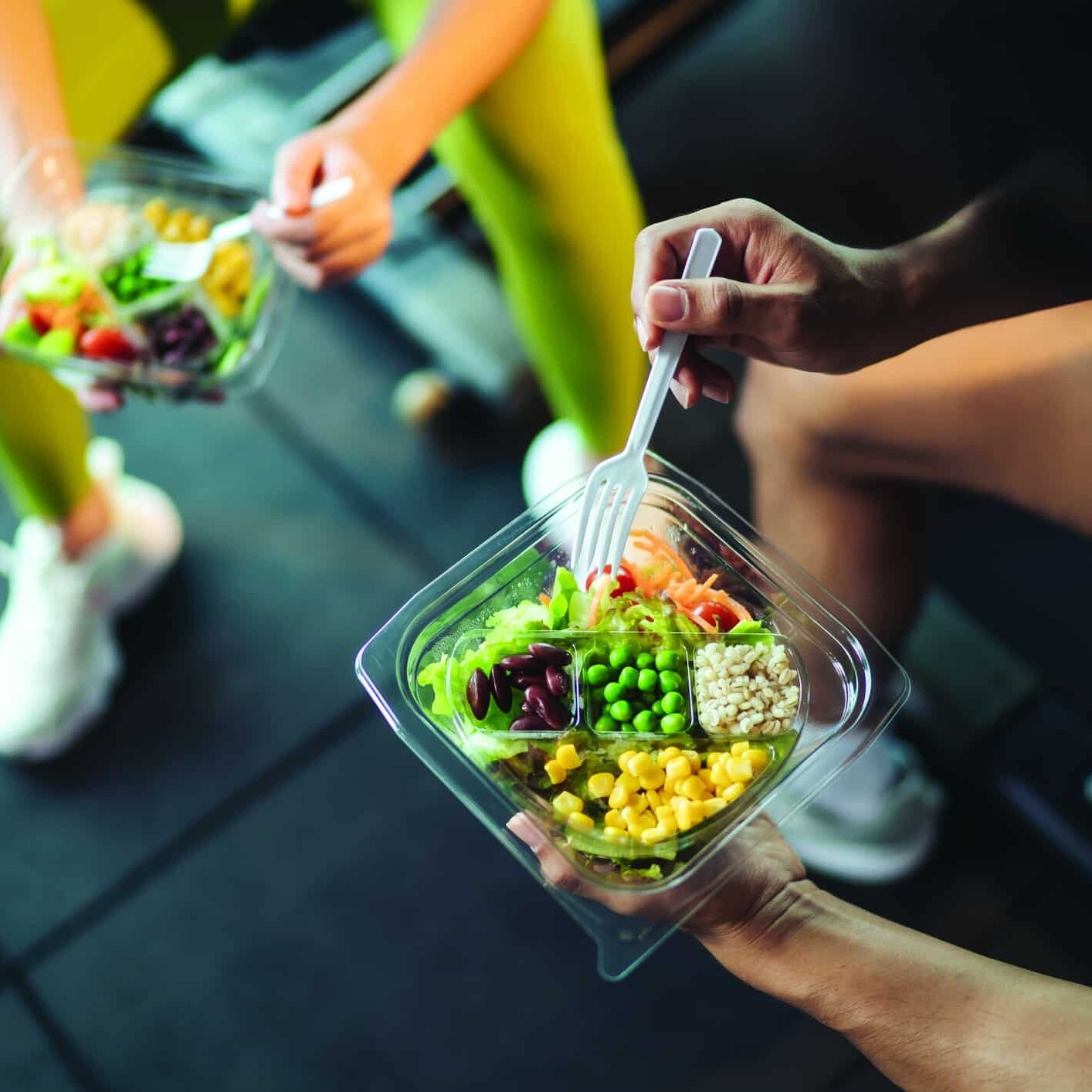 Top view Asian man and woman healthy eating salad after exercise at fitness gym. Two athlete eating salad for health together. Selective focus on salad bowl on hand.